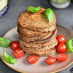 A stack of buckwheat pancakes on a brown plate with cherry tomatoes and basil leaves.