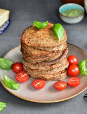 A stack of buckwheat pancakes on a brown plate with cherry tomatoes and basil leaves.
