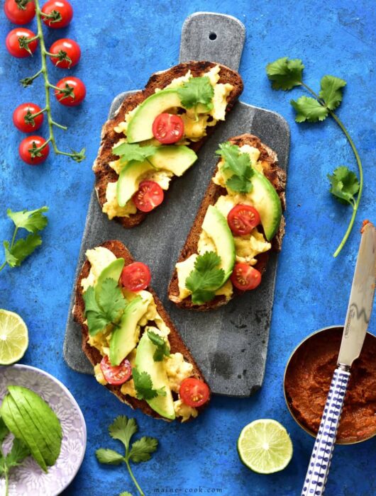 harissa, scrambled eggs and avocado toasts on a blue background