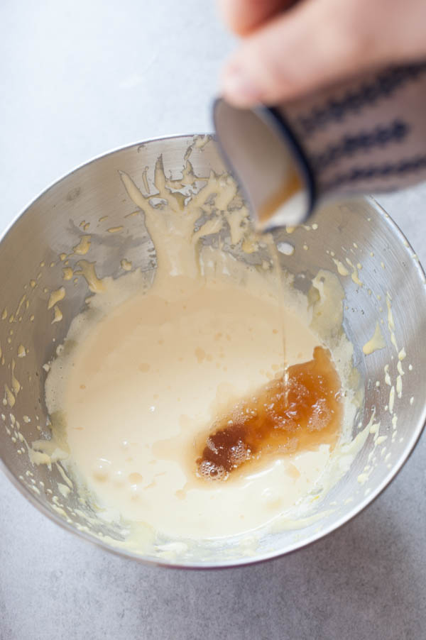 amaretto and vanilla extract are being poured into the beaten egg yolks with sugar
