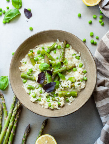 asparagus risotto with green peas in a green plate, asparagus and lemons in the background