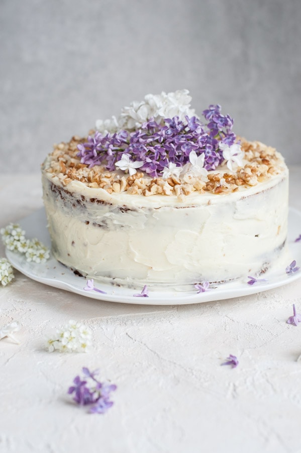 Carrot layer cake with cream cheese frosting on a white plate.