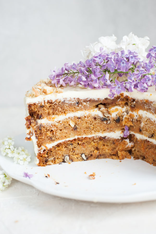 Close up picture of carrot layer cake with cream cheese frosting with a piece missing.