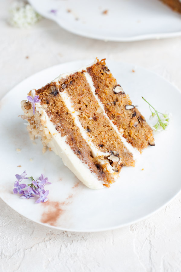 A piece of carrot layer cake with cream cheese frosting on a plate.