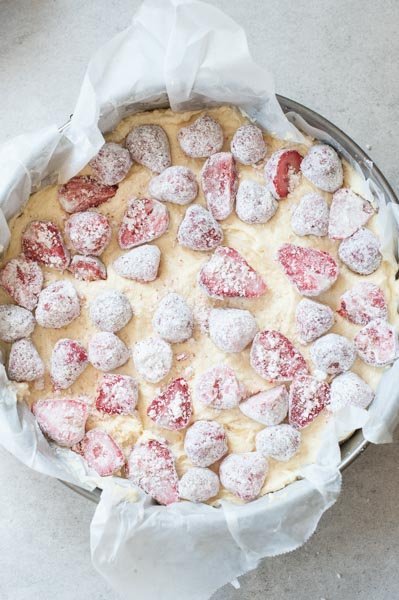 cornstarch covered strawberries scatter over coconut cake batter in a springform pan