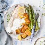 roasted trout with potatoes, asparagus and yogurt dip on a blue plate