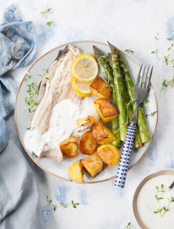 roasted trout with potatoes, asparagus and yogurt dip on a blue plate