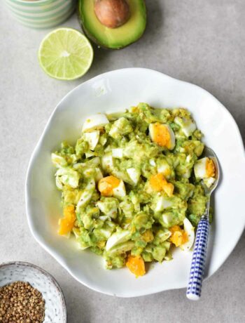 avocado egg salad in a white bowls, limes and coriander in the background