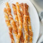 puff pastry cheese straws on a white plate, pumpkin soup in the background