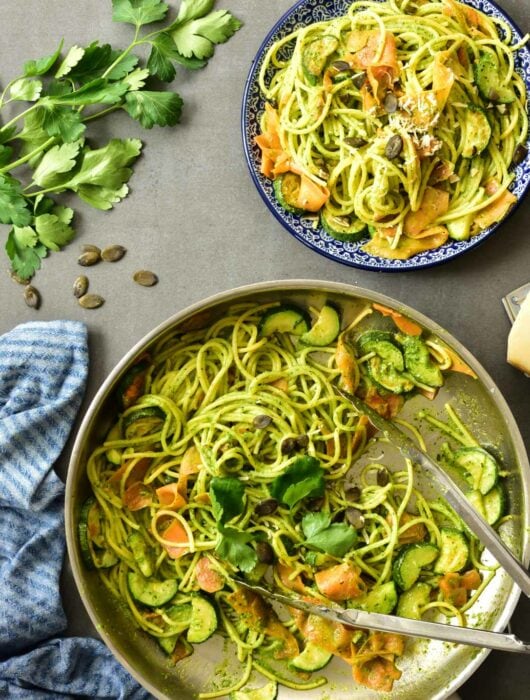 Parsley pesto pasta with zucchini and carrots in a pan.