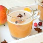 spiced apple cider in a glass, apples and spices in the background