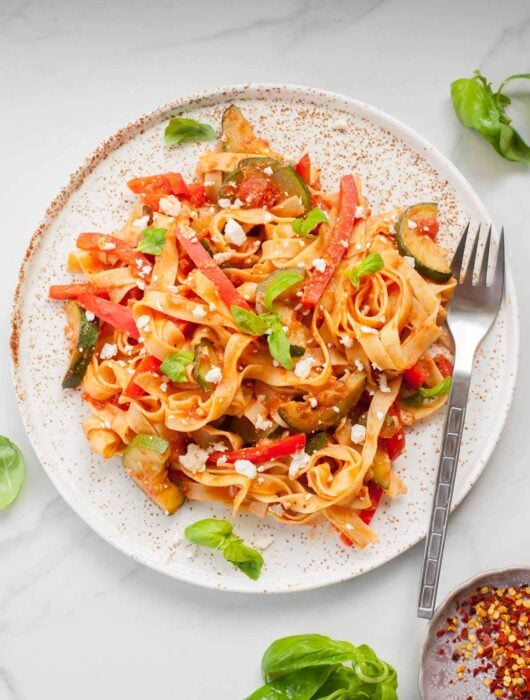 tagliatelle pasta with zucchini, bell pepper and feta on a white plate