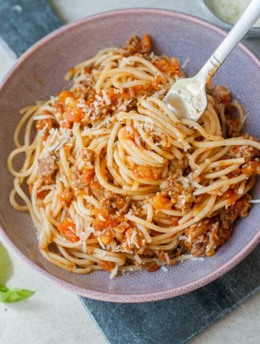 szybkie spaghetti z mięsem i sosem ze świeżych pomidorów nabite na widelec w fioletowej misce