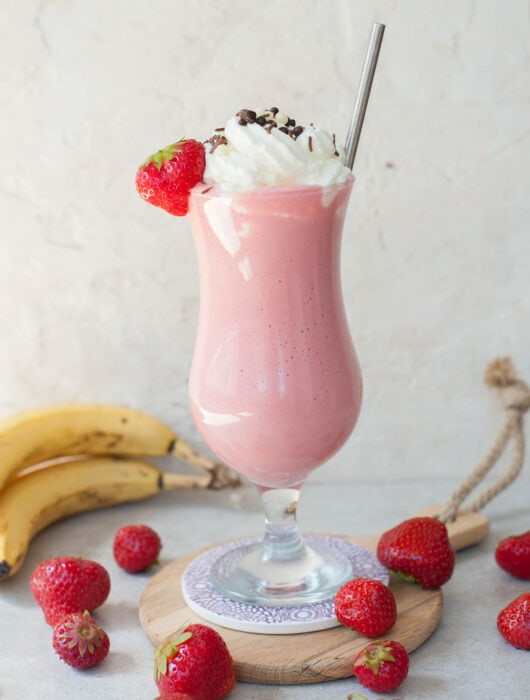 strawberry banana milkshake in a high glass with whipped cream