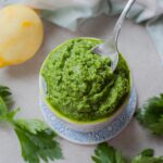 Celery leaf pesto being scooped with a teaspoon from a white ramekin.