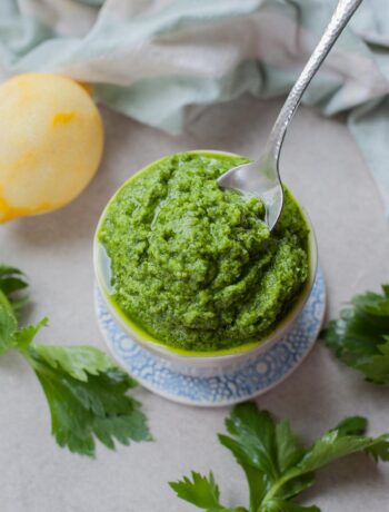 Celery leaf pesto being scooped with a teaspoon from a white ramekin.