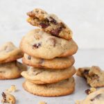 A stack of chocolate chip pecan cookies. Crumbled cookies scattered around.