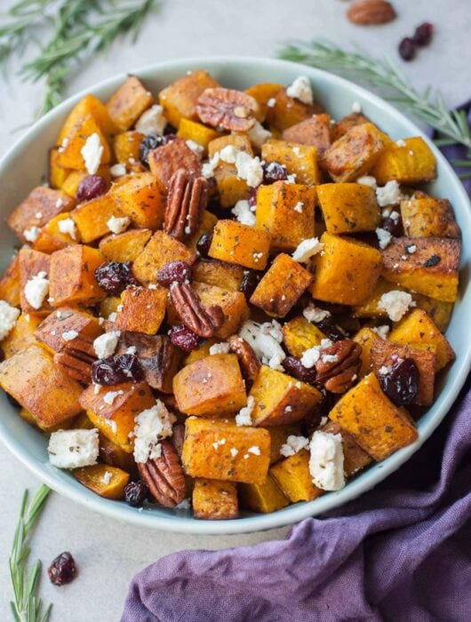 Roasted butternut squash with cranberries, pecans, rosemary and feta cheese in a blue bowl.
