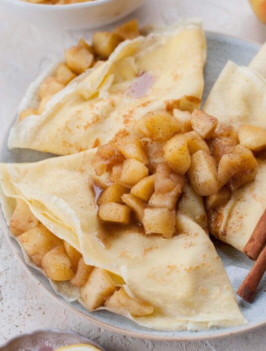 Apple crepes topped with sauteed apples on a blue plate.