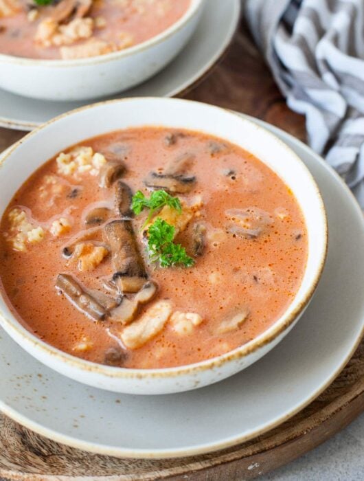 Chicken tomato soup with mushroom served with pasta and parsley in a white bowl.