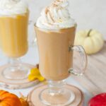 Two glasses with pumpkin spice hot chocolate topped with whipped cream and cinnamon sugar.