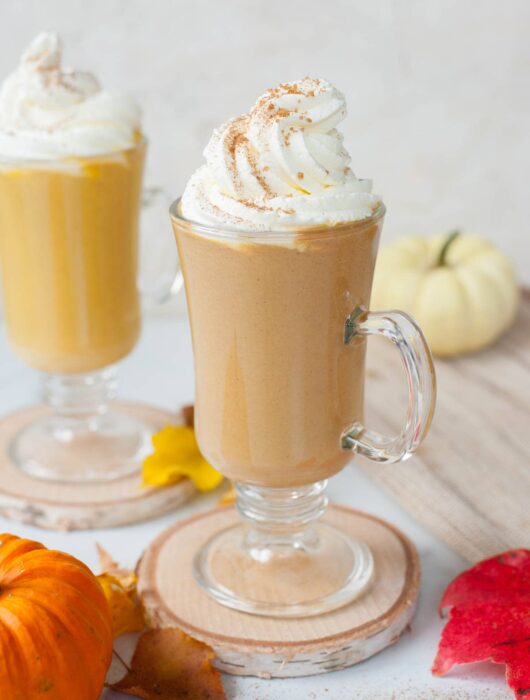 Two glasses with pumpkin spice hot chocolate topped with whipped cream and cinnamon sugar.