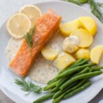 Salmon with creamy dill sauce, potatoes, and green beans on a blue plate.