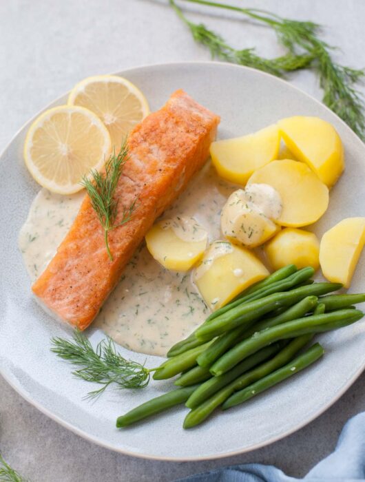 Salmon with creamy dill sauce, potatoes, and green beans on a blue plate.