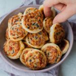 Puff pastry pinwheels with cheese, sun-dried tomatoes and olives in a violet bowl.