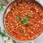 Chickpeas with chorizo in spicy tomato sauce in a silver frying pan.