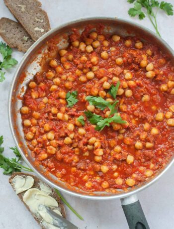 Chickpeas with chorizo in spicy tomato sauce in a silver frying pan.