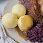 Potato dumplings on a brown plate with braised cabbage and roast goose.