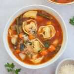 Two white bowls with vegetable tortellini soup.