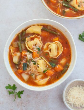 Two white bowls with vegetable tortellini soup.