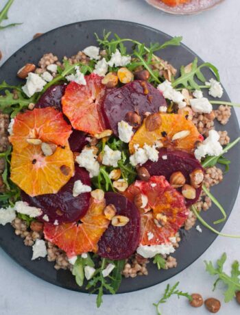 Buckwheat salad with beets, oranges, arugula, and feta cheese on a black plate.