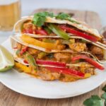 Chicken fajita quesadillas on a wooden boards topped with cilantro leaves.