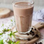 Coffee banana smoothie in a glass. Flowers and coffee beans on the side.