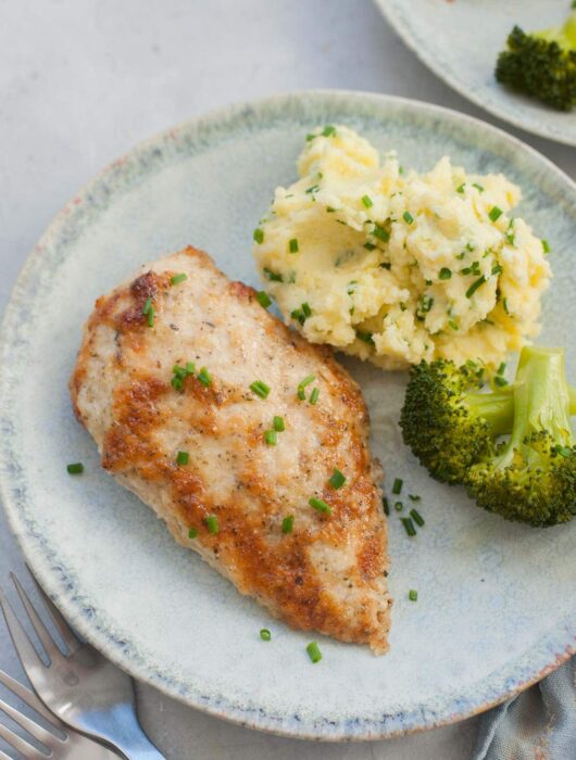 Parmesan mayo chicken on a green plate with mashed potatoes and broccoli.