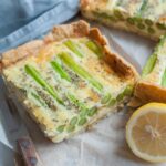 A piece of asparagus tart on parchment paper. Kitchen cloth and lemon in the background.