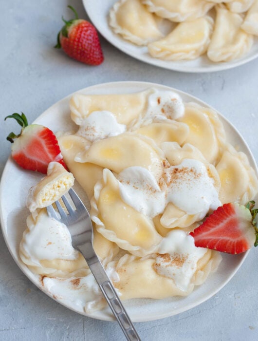 Pierogi on a white plate, topped with cream.