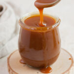 Salted caramel sauce in a jar is being spooned with a teaspoon.