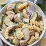 Chicken zucchini pasta in a white bowl is being picked with a fork.