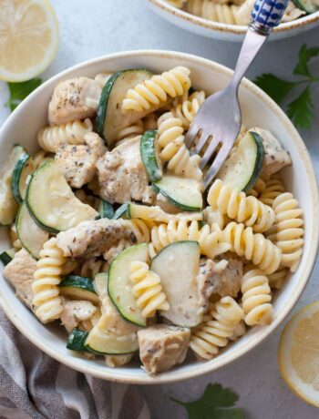 Chicken zucchini pasta in a white bowl is being picked with a fork.