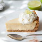 A slice of key lime pie on a white plate topped with whipped cream.