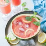 Watermelon mint lemonade in a watermelon half with ice cubes and lemon slices.