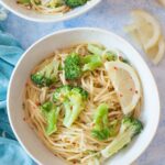 Lemon broccoli pasta in a white bowl. Lemon slices and parmesan cheese in the background.