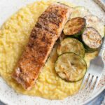 Saffron risotto with grilled salmon and zucchini on a white plate.