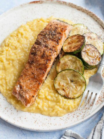 Saffron risotto with grilled salmon and zucchini on a white plate.