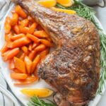 Whole roasted turkey leg on a white plate served with glazed carrots and potatoes.