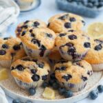 Blueberry muffins on a white plate. Blueberries and lemon slices scattered around.